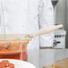 A person in a white coat using a Vollrath ivory oval spoodle to serve food from a container.