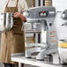 A person in a brown apron standing next to a Hobart Legacy+ commercial mixer with a bowl.