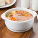 A stackable white porcelain soup bowl filled with soup with vegetables and meat on a table.