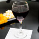 A Libbey red wine glass on a table with a napkin and cheese.
