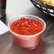 A Dart plastic souffle container filled with ketchup on a table.