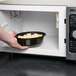 A hand holding a Pactiv Newspring VERSAtainer oval microwavable container full of food in a microwave.