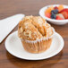 A muffin on a white Cambro polycarbonate plate with fruit in the background.