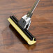A Rubbermaid wet mop with a yellow sponge on a wooden surface.
