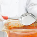 A person in white gloves using a Vollrath Orange Solid Oval Spoodle to serve sauce.