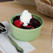 A Tuxton assorted color casserole dish filled with whipped cream and fruit with a spoon.