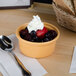 A Tuxton assorted color casserole dish filled with fruit and whipped cream with a spoon on the table.