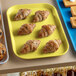 A yellow Cambro market tray of pastries on a bakery display table.