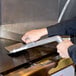 A person using a Nemco Heavy Duty Easy Grill Scraper to clean a metal grill surface.