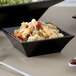 A black square melamine bowl filled with pasta and salad.