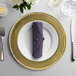 A 10 Strawberry Street gold charger plate with a purple napkin on it.