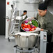 A man in a school kitchen using a Hobart 45 qt. food processor to prepare vegetables in a bowl.