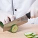 A person in white gloves uses a Mercer Culinary Nakiri knife to cut a cucumber on a table.
