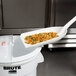 A white plastic Carlisle ice shovel scooping pasta into a bowl.