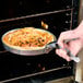 A hand using an American Metalcraft pizza pan gripper to put a pizza in an oven.