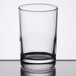 A clear Libbey side water glass with a white rim on a table.