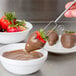 A person using an Ateco dipping tool to dip a strawberry in chocolate.