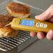 A hand holding a yellow Taylor digital folding thermocouple thermometer over chicken.