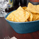 A blue oval basket filled with chips on a table.