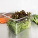 A Carlisle clear plastic food pan filled with lettuce and carrots on a counter.