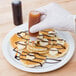 A hand using a Tablecraft Chef Squeeze Bottle to drizzle chocolate on banana slices.