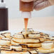 A Tablecraft squeeze bottle pouring syrup onto a plate of pancakes.