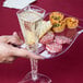 A hand holding a Fineline clear plastic cocktail plate with a glass of champagne and food on it.