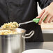 A person using a Vollrath Jacob's Pride Heavy-Duty Solid Basting Spoon with a green Ergo Grip to serve pasta.