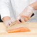 A person in gloves uses a Dexter-Russell DuoGlide chef knife to cut a piece of salmon.