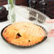 A person using a D&W Fine Pack black plastic container with a clear high dome lid to cover a pie.