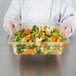 A chef holding a Cambro amber plastic food pan full of vegetables.