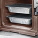 A dark brown Cambro Ultra Pan Carrier on a counter holding food trays.