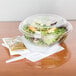 A Dart clear plastic bowl filled with salad on a table with a fork.