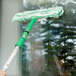 A hand holding a Unger Monsoon Plus T-Bar mop with a green handle cleaning a window.