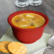A Fiesta Scarlet China bouillon bowl filled with soup and crackers on a napkin.