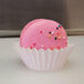 A white fluted mini baking cup with a pink macaron and sprinkles on top.