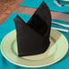 An Intedge black cloth napkin folded on a plate.