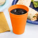 A Sunkissed Orange plastic cup filled with ice water next to a plate of food.