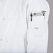 A person wearing a Mercer Culinary Millennia white chef coat with a pocket full of pens and a phone.