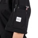 A person wearing a black Mercer Culinary Millennia Air short sleeve cook jacket with a phone and pen in the pockets.