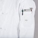 A person wearing a Mercer Culinary Millennia white chef coat with a pocket full of tools and a cell phone.