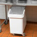 A white plastic Baker's Mark ingredient bin with a clear sliding lid on top of a white table.