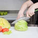 A hand holding a Mercer Culinary Millennia Colors chef knife cutting vegetables on a cutting board.
