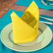 A folded yellow Intedge cloth napkin on a plate.