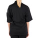 A woman wearing a Mercer Culinary black short sleeve chef jacket with a mesh back.