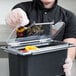 A person in black gloves using a Carlisle Coldmaster food container lid to cover food on a counter.