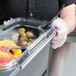 A person wearing plastic gloves uses a Carlisle Coldmaster food pan lid to hold a container of food at a salad bar.