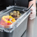 A person using a Carlisle clear plastic food pan lid to hold a container of peppers and olives.