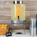 A Cal-Mil Soho glass beverage dispenser with an infusion chamber filled with orange juice and fruit.