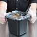A person in gloves using a Carlisle clear plastic food pan lid to cover a container of food.